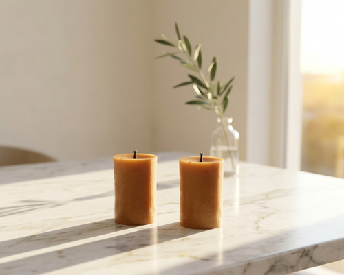Two amber-colored beeswax candles on a marble surface with a blurred background