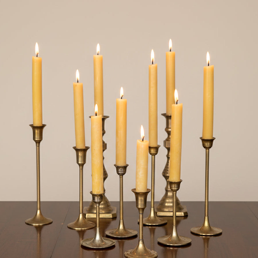 Set of lit beeswax candles on brass candlesticks against a plain background